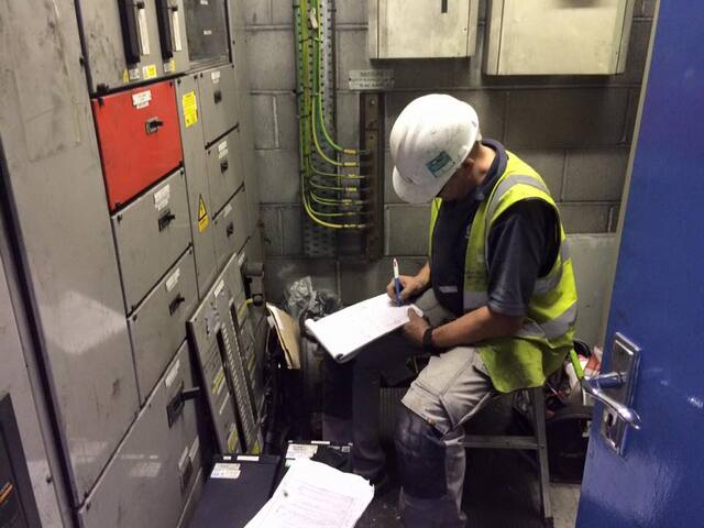 Engineer writing notes beside industrial switchgear